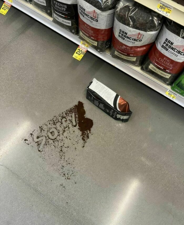 Spilled coffee grounds on store floor forming the word sorry next to a torn coffee bag on the shelf aisle.