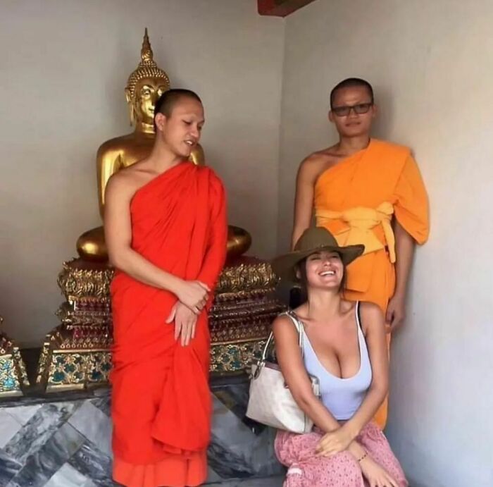 Two monks in orange robes standing next to a smiling woman in a hat, an awkward photo at a temple setting.