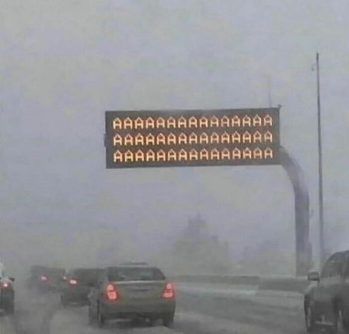 Highway sign displaying repeated letter A's on a foggy day, capturing an awkward photo moment on a busy road.