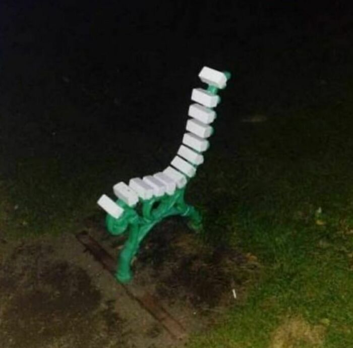 Bench with uneven and awkwardly placed white slats creating a painful and uncomfortable appearance at night outdoors