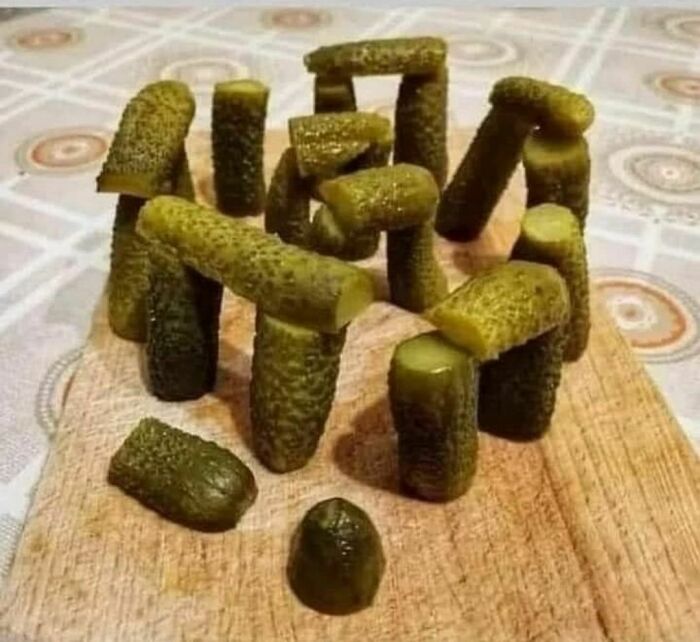 Pickles arranged awkwardly to resemble a miniature Stonehenge on a wooden cutting board, creating an uncomfortable visual.