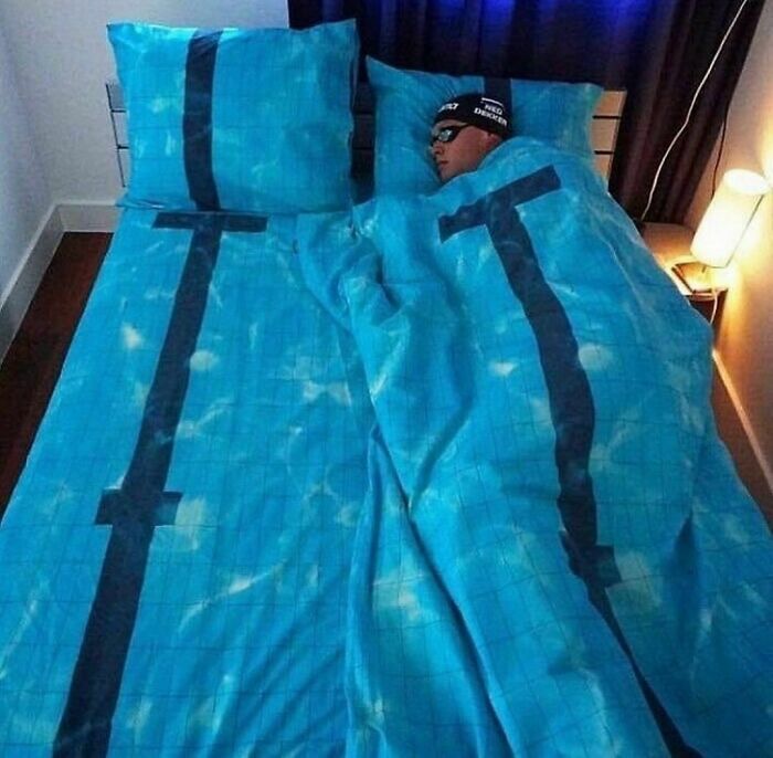 Man sleeping in a bed with blue bedding designed to look like a swimming pool lane, creating an awkward photo moment.