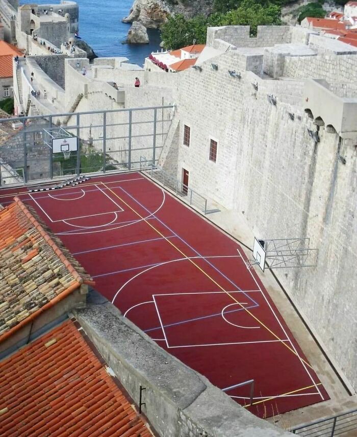 Awkward basketball court squeezed between ancient stone walls with uneven playing surface and obstructed hoop.