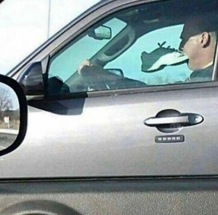 Man driving a car with a torn window that looks like something is biting his face in an awkward photo moment.