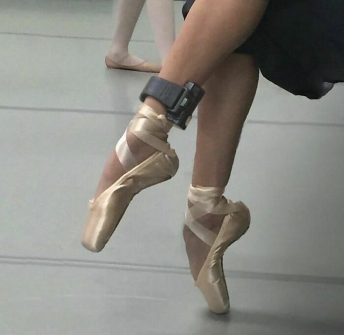 Ballerina's feet in pointe shoes with an ankle monitor, highlighting an awkward photo moment in dance practice.