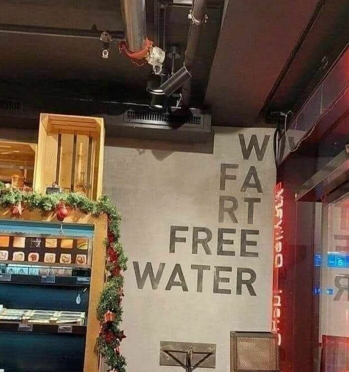 Sign on wall with awkwardly arranged letters spelling words including fart and free water in a restaurant setting.