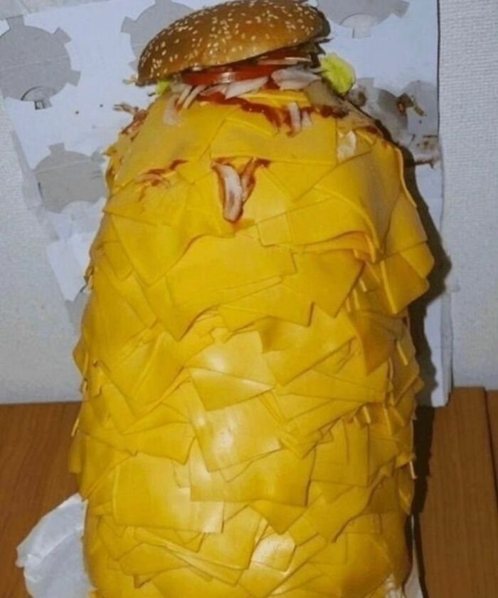 Awkward photo of a hamburger overloaded with slices of cheese, creating an almost painful visual experience.
