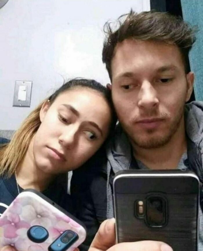 Couple sitting close, both looking at their phones with serious expressions in an awkward photos moment.