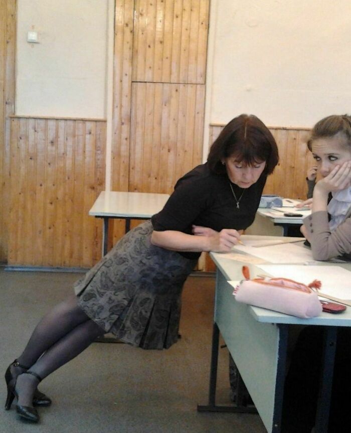 Woman leaning at an impossible angle while writing on a desk, creating an awkward photo moment in a classroom setting.