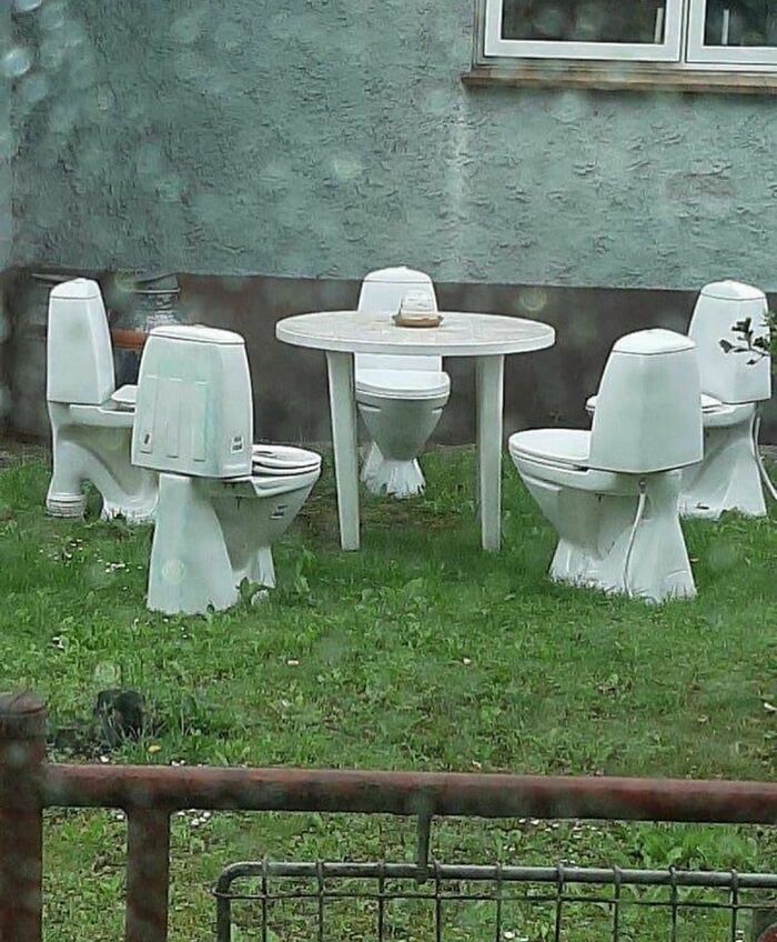 Outdoor seating area with toilets used as chairs around a round table, creating an awkward photo scene.