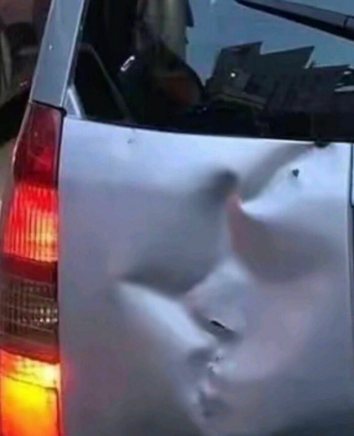 Damaged silver car door with a large dent creating an awkward and almost painful visual effect on the metal surface.