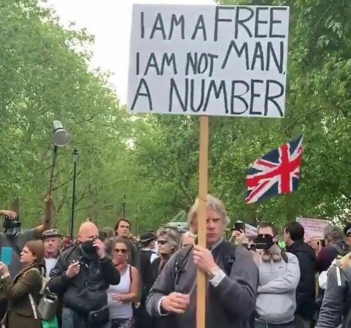 Man holding awkward protest sign at crowded outdoor event, illustrating awkward photos that are painful to look at.
