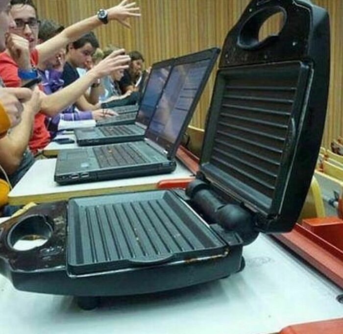 Students in a classroom with laptops, while a sandwich press is awkwardly placed on a desk, creating an awkward moment.