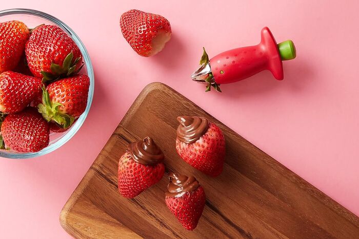 Strawberry huller and chocolate-filled strawberries on a wooden board, one genius Amazon find solving kitchen problems.