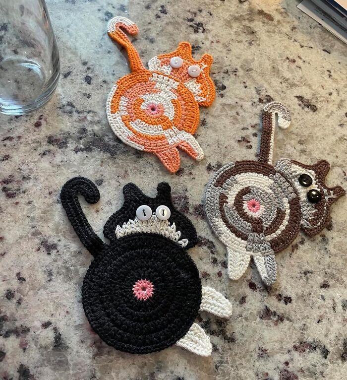 Crocheted cat coasters with button eyes on a granite countertop, highlighting unique and weird things.