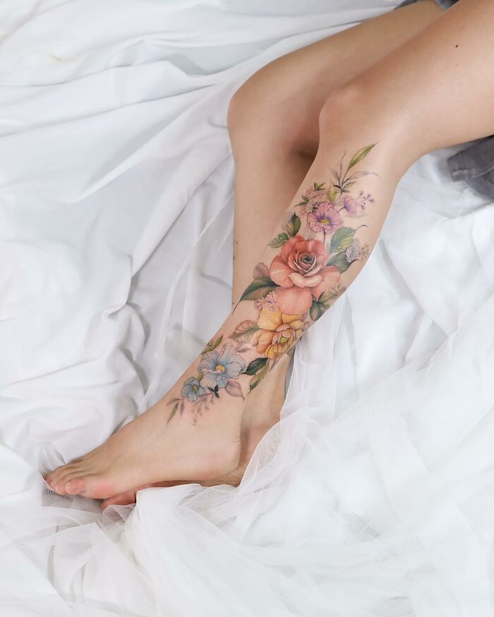Watercolor-style floral tattoo on a leg, featuring roses and petals, showcasing delicate, artistic design.