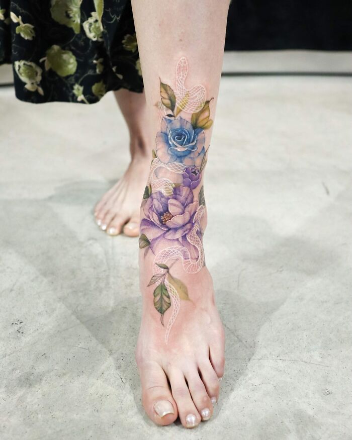 Watercolor-inspired tattoo with blue roses and a snake on a person’s leg.