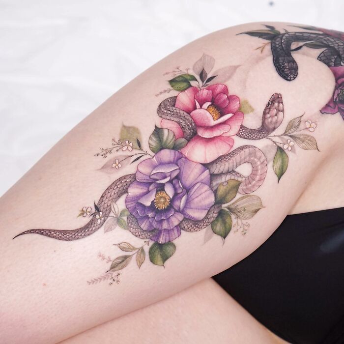 Watercolor-style tattoo design with snakes and colorful flowers on skin.