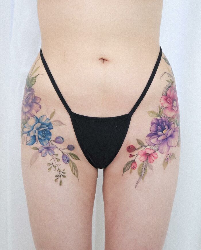Watercolor-inspired floral tattoos on thighs, showcasing intricate designs by talented artist.