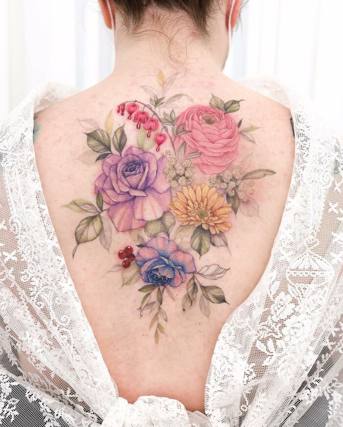 Watercolor-style tattoo design of vibrant flowers on a person's back, framed by a lace garment.
