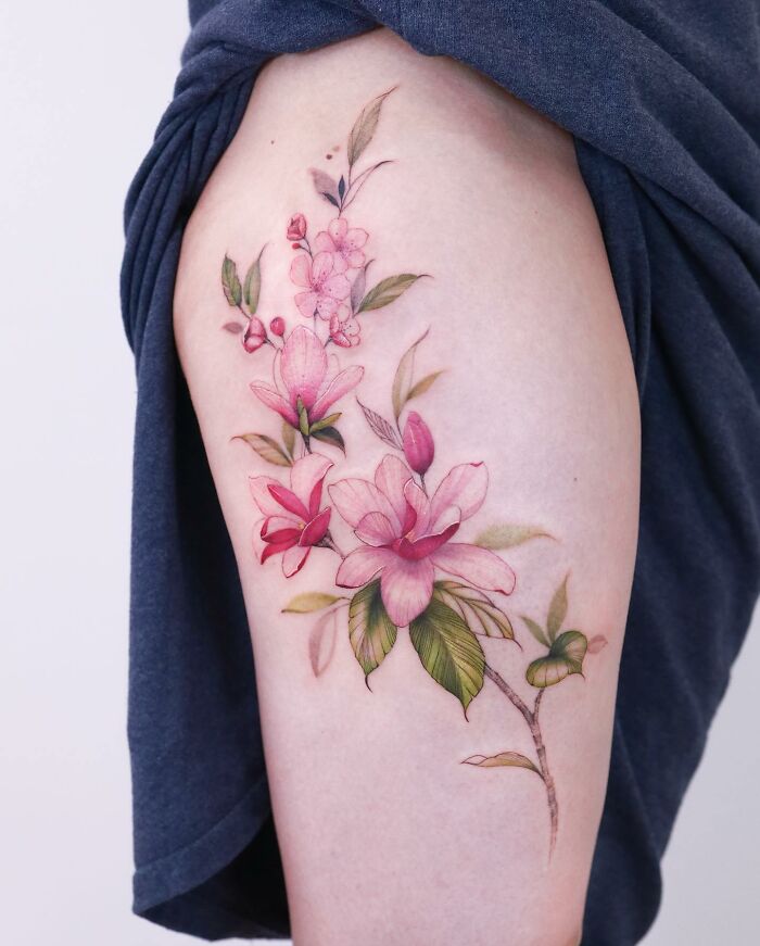 Watercolor style tattoo of pink flowers on a person's thigh.