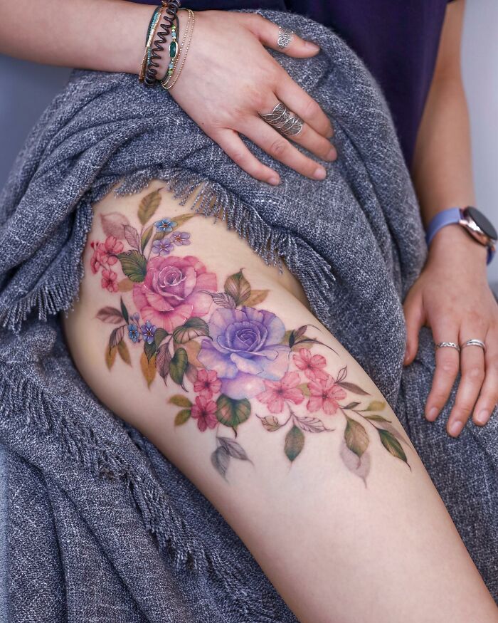 A vibrant floral tattoo on a thigh, designed with watercolor painting techniques.