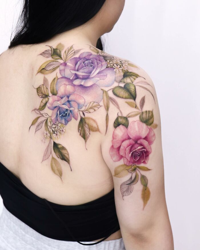 A tattoo design on a woman's back features watercolor-style roses and leaves.