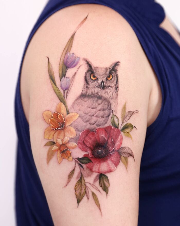 Watercolor-style tattoo of an owl with colorful flowers on an arm.