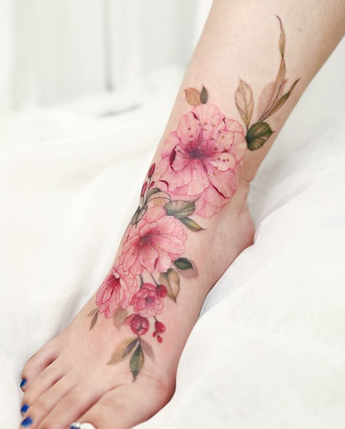 Watercolor tattoo design of pink flowers and green leaves on a person's foot.