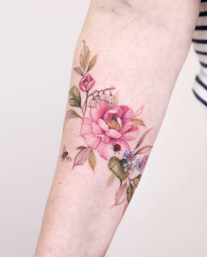 Watercolor tattoos featuring a pink flower and small insect details on an arm.