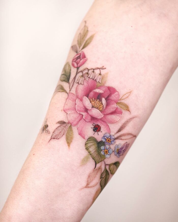 Watercolor-style tattoo design featuring pink flowers with green leaves and small insects on the forearm.