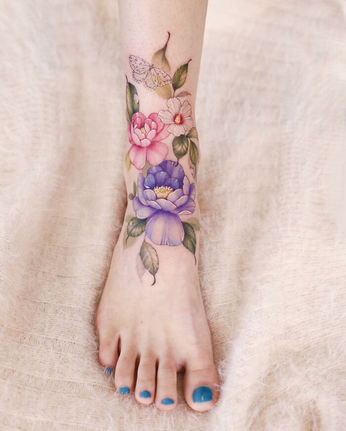 Watercolor tattoo design on ankle with vibrant flowers and a delicate butterfly.