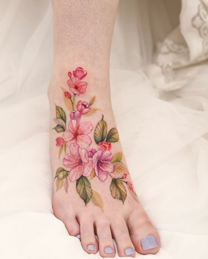 Watercolor tattoo design of pink flowers and green leaves on a person's foot, showcasing the vibrant artistry.