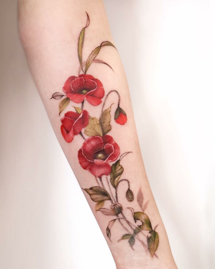 Watercolor tattoo design of red flowers and green leaves on an arm.