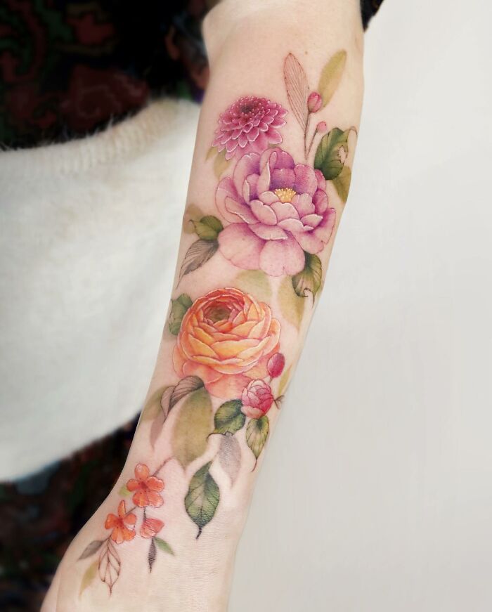 Watercolor-inspired tattoo design on forearm featuring vibrant flowers and leaves.