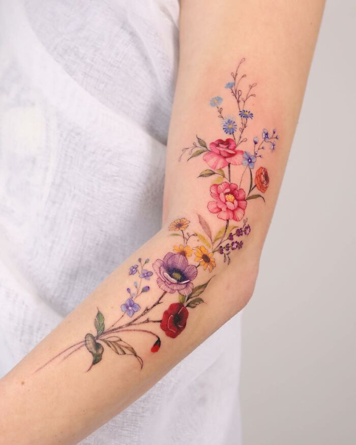Arm adorned with a floral tattoo design, reminiscent of watercolor painting, showcasing vibrant colors and delicate details.