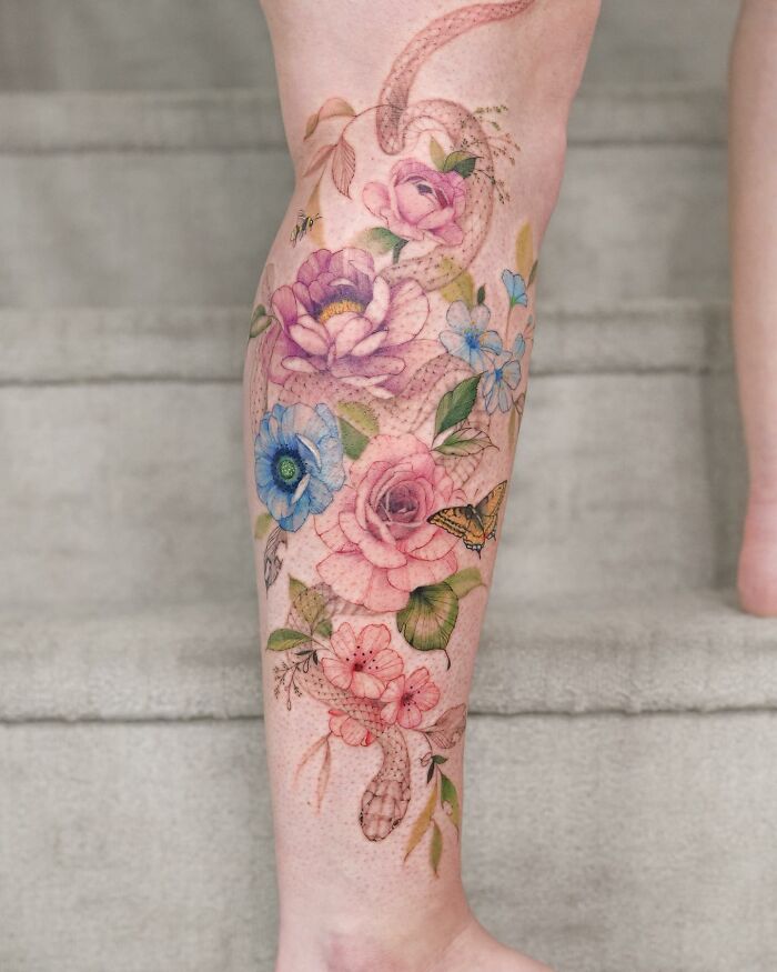 Watercolor tattoo design featuring colorful flowers and a butterfly on a person's leg.