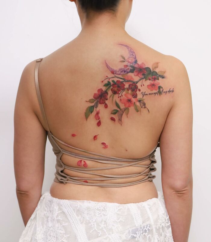 Watercolor-inspired tattoo featuring flowers and a crescent moon on a woman's back.