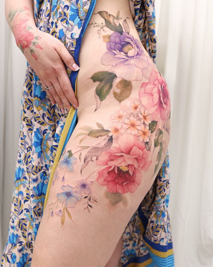Watercolor tattoo design on a thigh, featuring vibrant flowers, reminiscent of a painting.