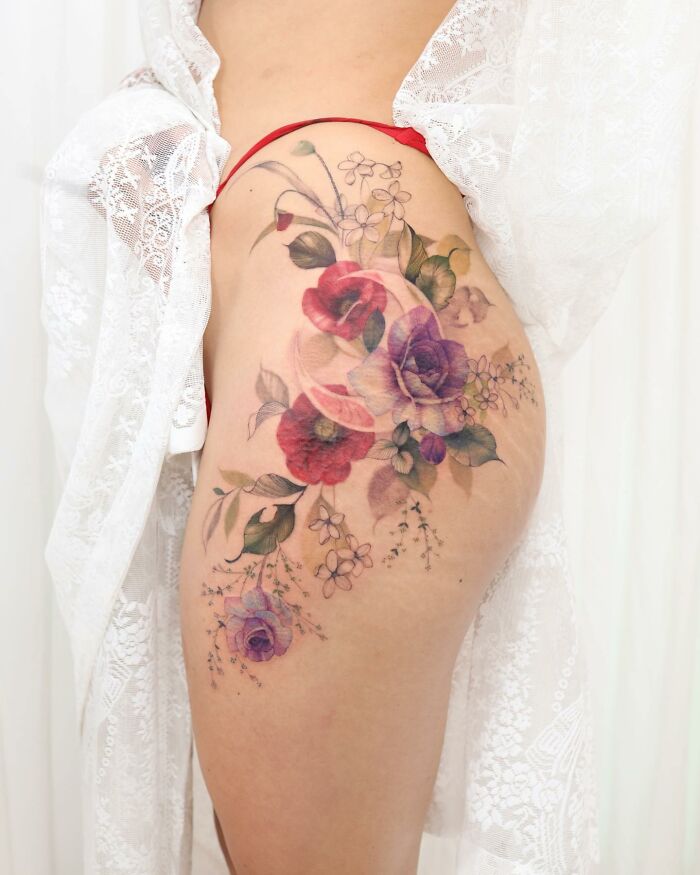 Watercolor tattoo design featuring vibrant flowers on a person's upper thigh.
