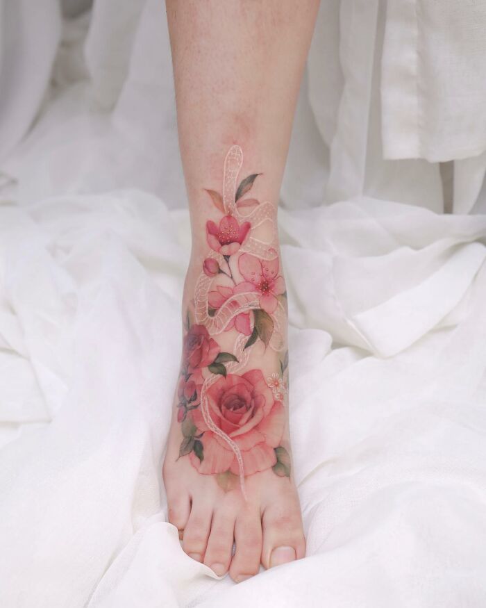 Watercolor painting-inspired tattoo featuring pink roses and leaves on a person's foot.