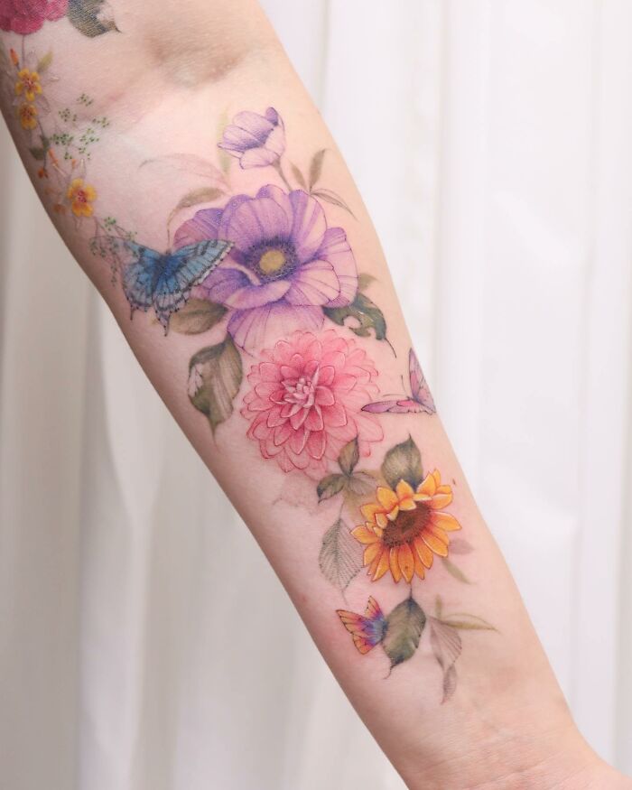 Watercolor tattoo design featuring colorful flowers and butterflies on an arm.