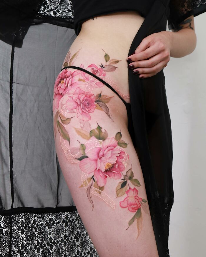 Watercolor-style tattoo of pink flowers on a person's thigh, illustrating artistic tattoo designs.