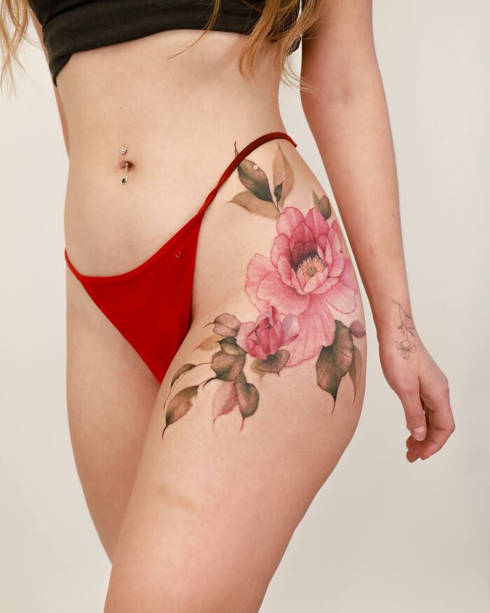 Watercolor-inspired tattoo of pink flowers on a woman's hip, wearing red underwear.
