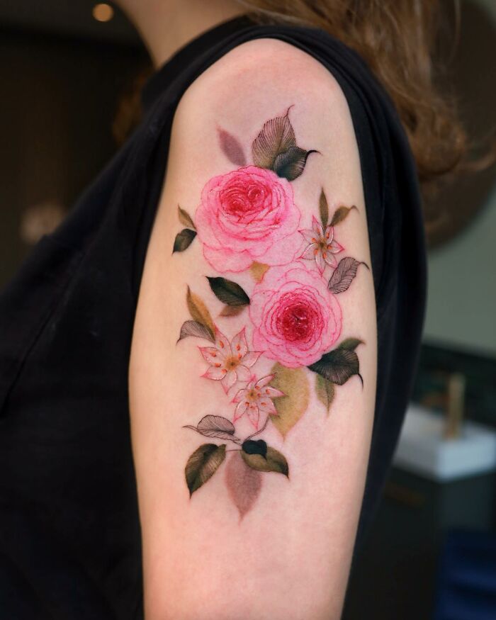 Floral tattoo design in watercolor style on upper arm, featuring pink roses and leaves.