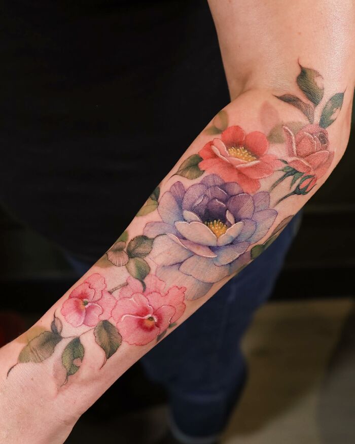 Watercolor-style tattoo featuring vibrant floral designs on a person's forearm.