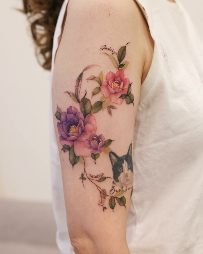 Watercolor tattoo design featuring colorful flowers and a cat on a person's arm.
