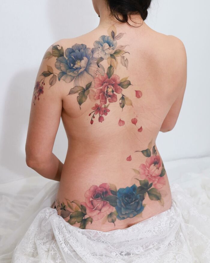 Woman with floral tattoos reminiscent of watercolor paintings on her back.