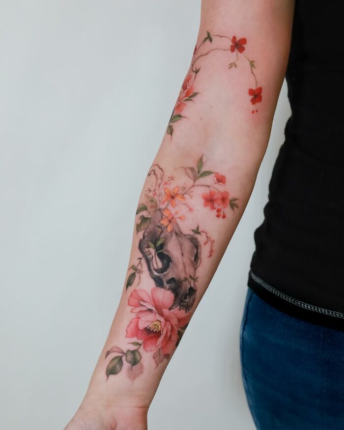 Watercolor-style tattoo with floral and skull elements on a person's forearm.