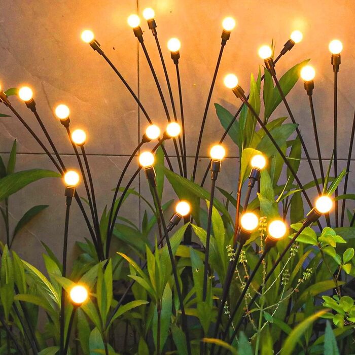 Illuminated garden lights resembling flowers among green plants at dusk, ideal for low-maintenance gardening style.